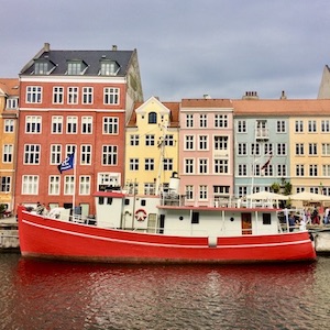 Pastel-colored buildings line a canal. A red and white boat sits in the water in front of them.