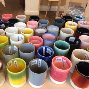 Many colorfully glazed tumblers are crowded together on a store shelf.