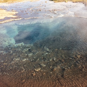 An aqua-colored hot spring with steam floating above the water.