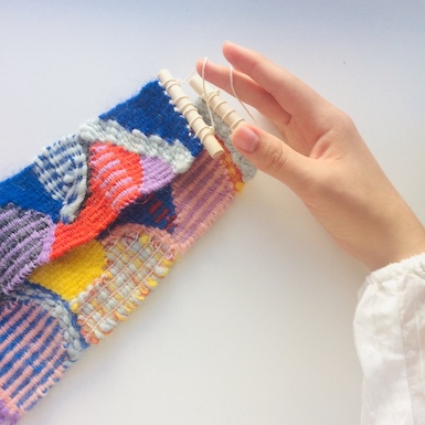 A hand holding two small, oblong weavings.