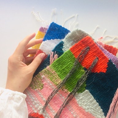 A hand beside four medium-sized weavings in bright colors.