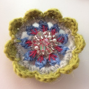 Crocheted flower with light green outer petals, blue and pink inner petals and clear glass beads in the center.