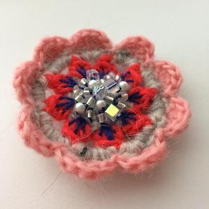 Crocheted flower with light pink outer petals, blue and red inner petals and clear glass beads in the center.