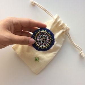 Blue felt circle embroidered with a radial pattern using glass beads in green, light blue, gold and pink.