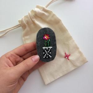 Cactus with a small pink sequin flower in a black and white basket with a diamond pattern.