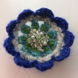 Crocheted flower with cobalt blue outer petals, green and aqua inner petals and clear glass beads in the center.