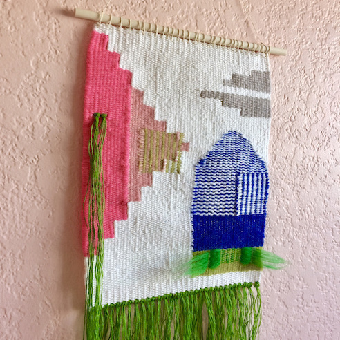 Square weaving, featuring geometric shapes, horizontal and vertical stripes and fringe. In green, pinks, cobalt, gray and white.