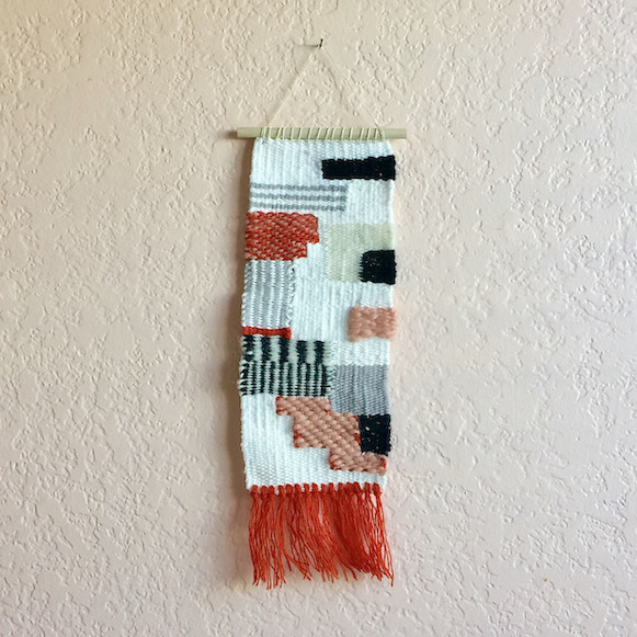 Rectangular weaving with geometric shapes, varigation, horizontal and vertical stripes. In orange, blush, gray, cream, black and white.